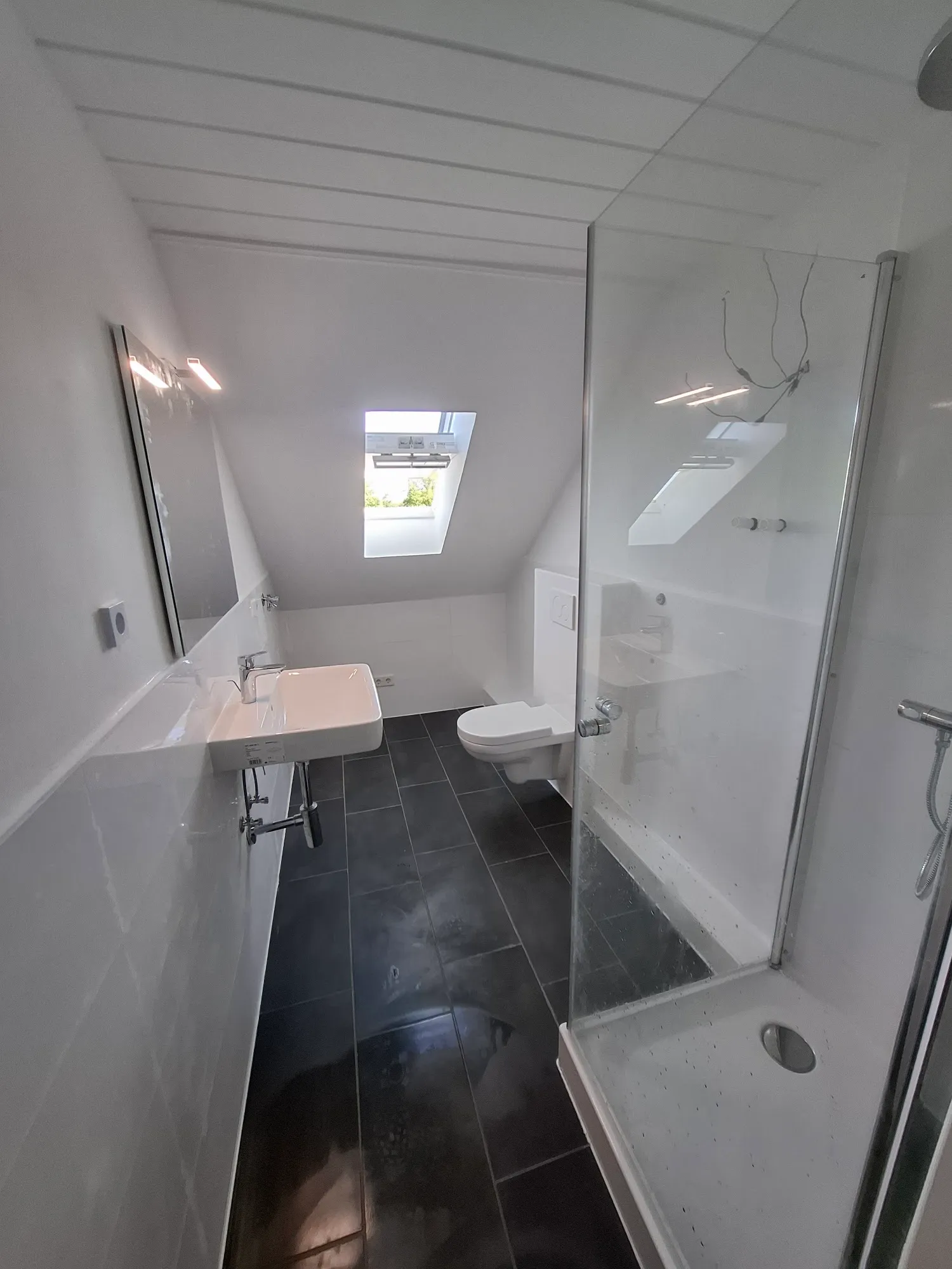Fertiggestelltes helles Badezimmer mit Dachfenster und Glasdusche