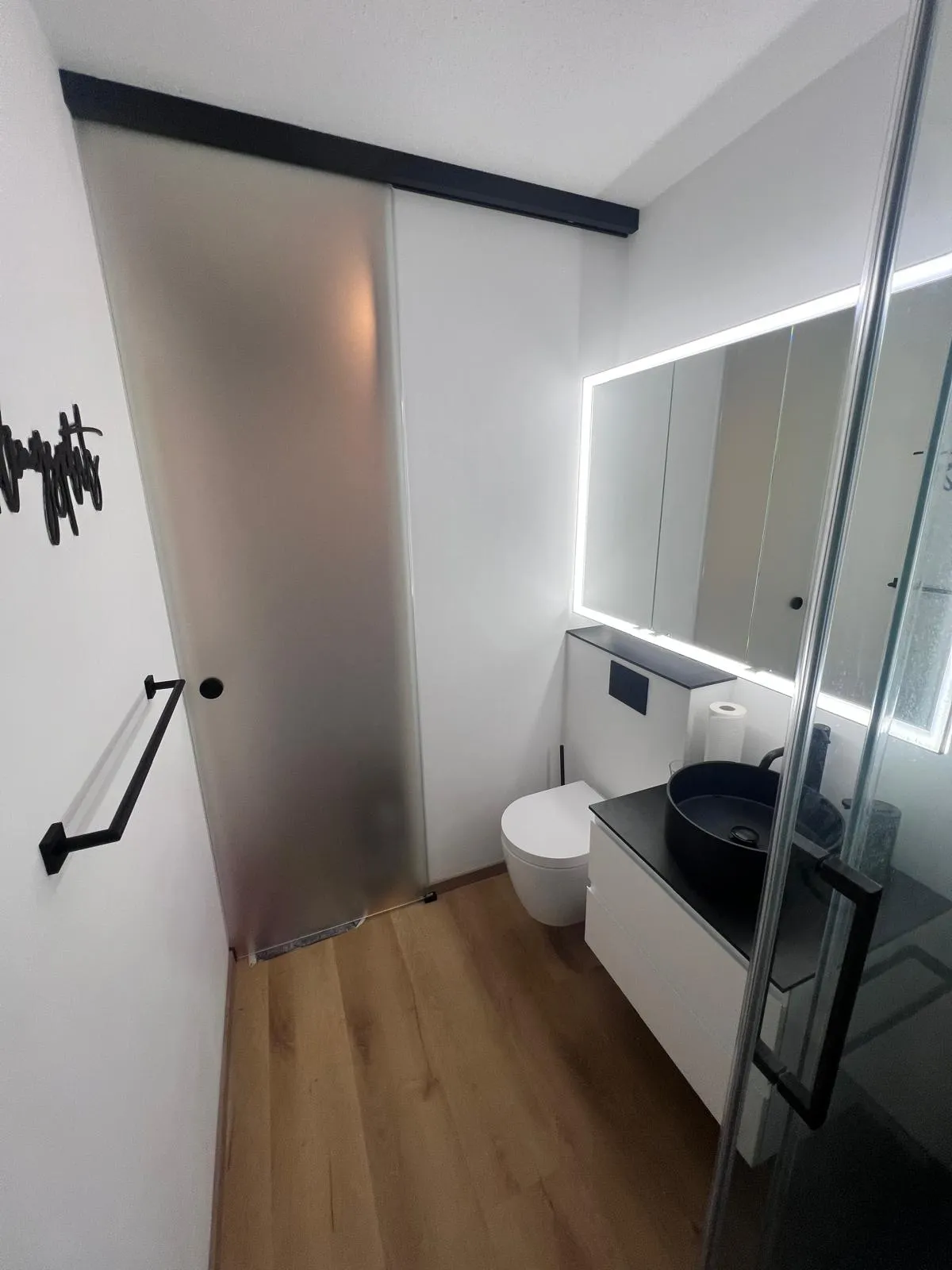 Elegantes Gästebad mit beleuchtetem Spiegel und dunklen Wandfliesen