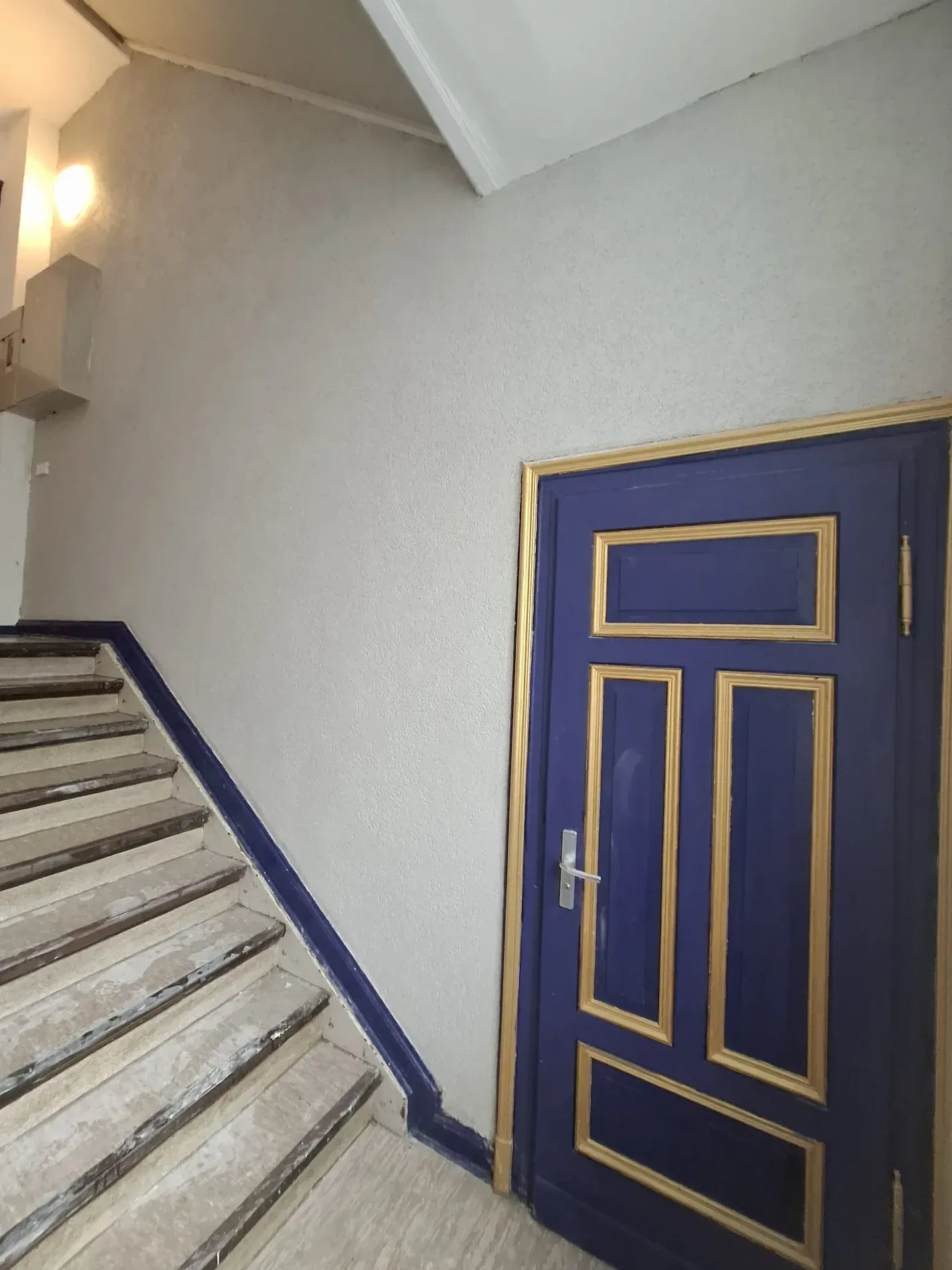 Dasselbe Treppenhaus nachher: fertig verputzte und gestrichene Wand neben der blauen Wohnungstür